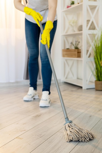 Cleaning company Female janitor Housework service Room hygiene Unrecognizable woman in protective gloves wiping washing laminated floor with mop light interior