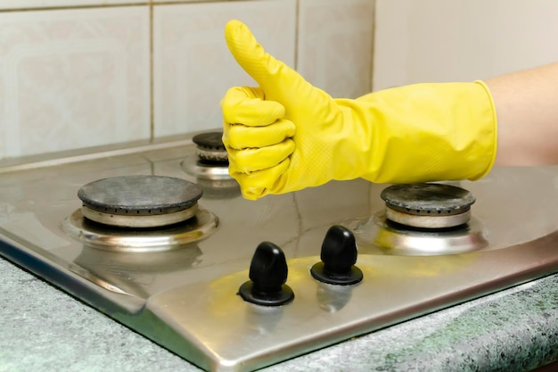 Очистка грязной газовой плиты от жира, остатков пищи. женская рука в защитной перчатке, моющей кухонную плиту. концепция уборки дома