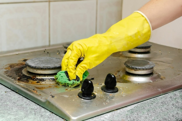 Cleaning dirty gas stove from grease, food leftovers deposits. woman's hand in protective glove with sponge rag and detergent washing kitchen stove. home cleaning service concept