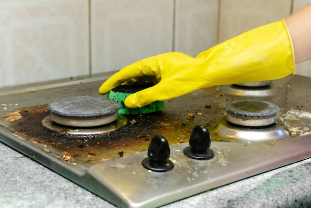 Cleaning dirty gas stove from greasefood leftovers depositshand in glove sponge rag kitchen stove