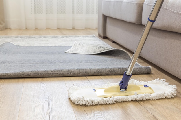 Cleaning floor with mop under carpet in living room