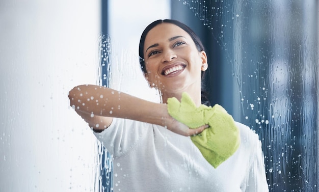 Cleaning glass and hygiene with a black woman using a cloth or rag while wiping a window in an office Cleaner janitor or housekeeper washing a transparent surface with soap and water