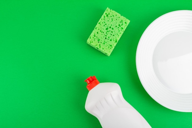 Photo cleaning green sponge white plate and detergent for dishes on a green background top view flatlay