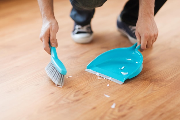 Pulizia e concetto di casa - primo piano del pavimento in legno per scopare  maschi con piccola scopa a frusta e paletta