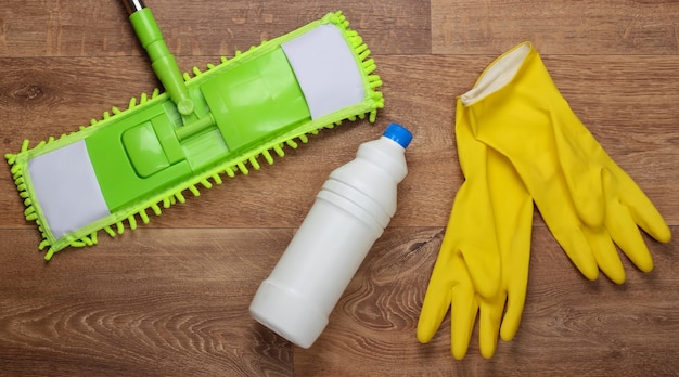 Prodotti per la pulizia. mop verde di plastica, guanti, bottiglia di detersivo sul pavimento di legno. disinfezione e pulizia in casa. vista dall'alto