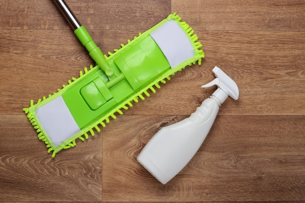 Cleaning products. Plastic green mop, spray bottle on wooden floor. Disinfection and cleaning in the house. Top view