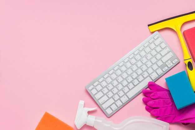 Cleaning products, rubber gloves, sponges, window scraper and keyboard on a pink background. Concept call of a cleaning company via the Internet, online training. Flat lay, top view