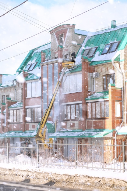 Il servizio di pulizia pulisce la neve dal tetto della casa. i lavoratori su attrezzature speciali puliscono la neve in inverno. pulizia del ghiaccio e della neve dai tetti delle case.