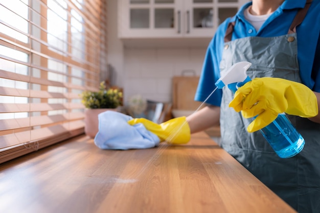 Cleaning service Closeup of woman in apron and rubber gloves cleaning wooden table with spray