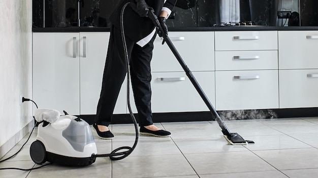 전문 스팀 청소기 장비로 주방 바닥에서 먼지를 제거하는 청소 서비스 회사 직원
