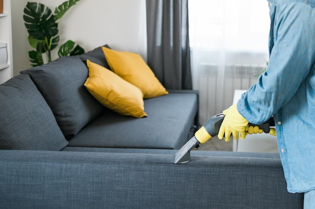 Сотрудник клининговой компании удаляет грязь с мебели в квартире с помощью профессионального оборудования м