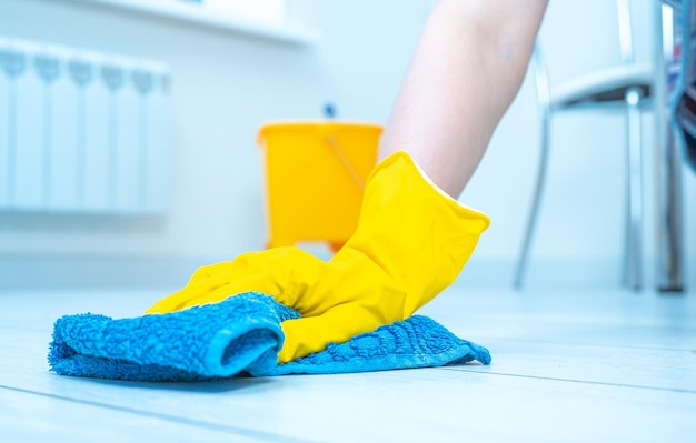 Cleaning service crop image of woman thoroughly and gently\
washing and cleaning white laminate floor female hands in yellow\
gloves wipe wooden floor with blue microfiber cloth copy space