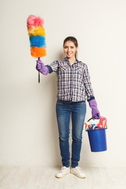 Cleaning services concept. Young woman holding bucket with detergents and rags at white isolated background. Household and home cleaning