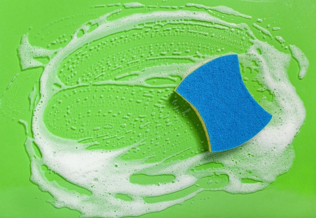 Фото Чистящая губка, вытирающая мыльную пену на зеленом фоне, концепция бытовой стирки