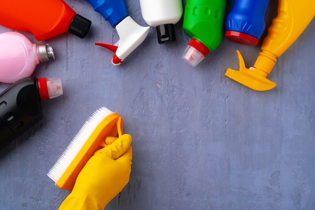 Cleaning supplies with hands in rubber gloves on gray background