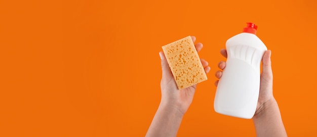 Cleaning yellow sponge and detergent for dishes holding in hand on a yellow background