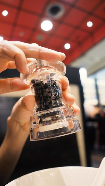 Vetro di colore trasparente e macinapepe nero thailandese o macinacaffè nelle mani che torcono la bottiglia