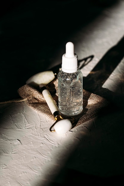 A clear glass dropper bottle with serum, oil, and hyaluronic acid, one woodcut in sunlight.