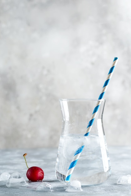 Clear water with ice in a glass with a straw and cherries