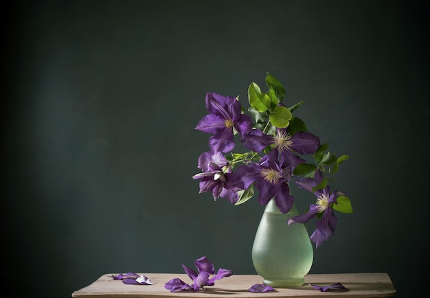 Clematis bloemen in glazen vaas op vintage houten plank