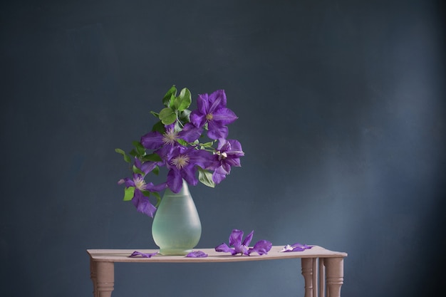 Clematis bloemen in glazen vaas op vintage houten plank