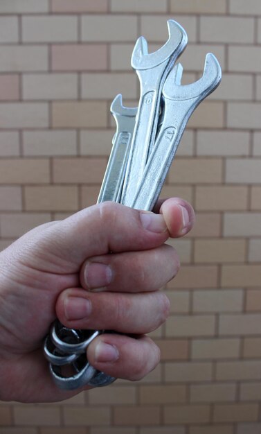 Photo clenched human fist with different open end wrenches over brick wall