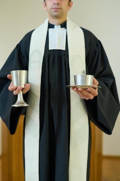 Sacerdote in tonaca con colletto clericale che regge coppe con roba da comunione