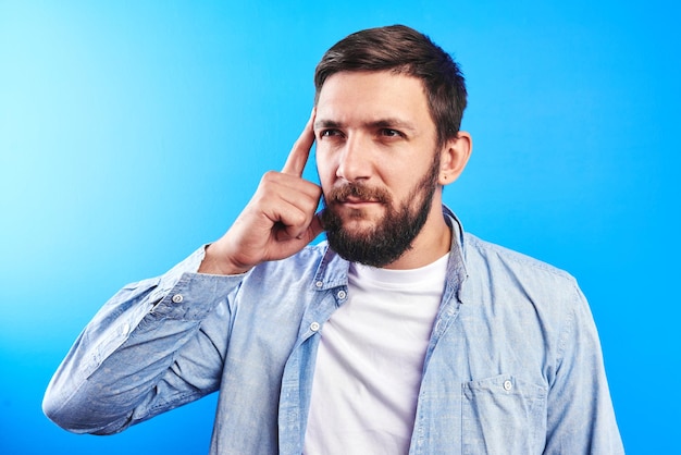 Clever bearded man shows finger on the smart head, brain and mind, encourages you to think well isolated in blue studio