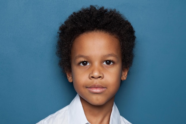 Clever black child student boy looking at camera on blue background close up portrait