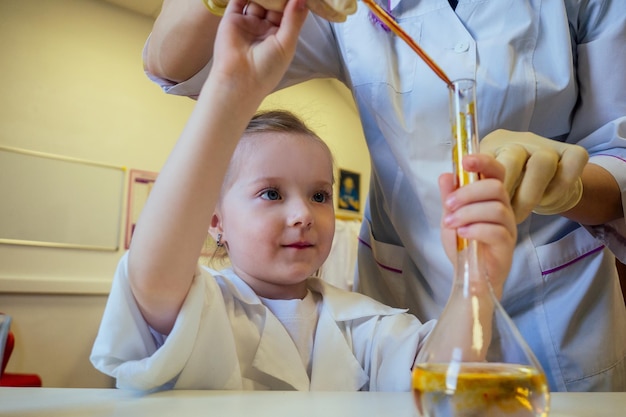 Clever blonde school girl chemist in eyeglasses and white medical gown making science experiments chemistry ,mixing different chemical solutions in laboratory classroom