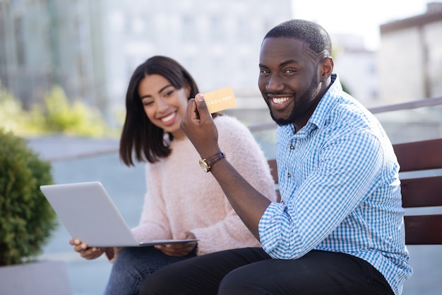 Clever dedicated innovative man enjoying a day outside with his girlfriend and paying for the goods she choosing online with his credit card