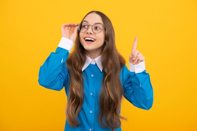 Clever idea Clever girl in eyeglasses yellow background School age child with raised finger Eureka Basic education