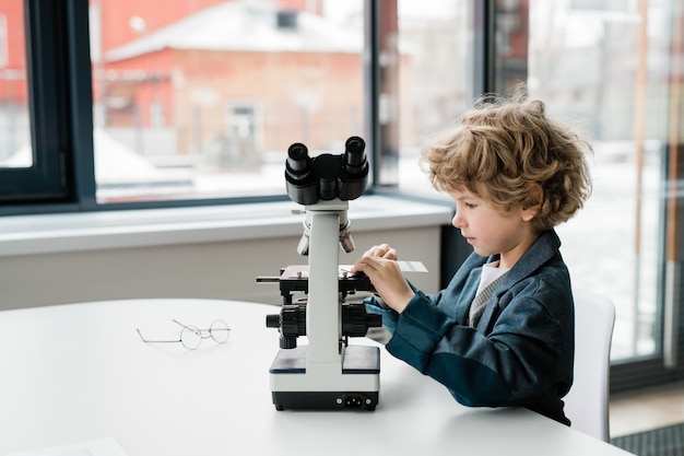 Foto piccolo scienziato intelligente che mette campione chimico nel microscopio mentre studia nuovi elementi in laboratorio