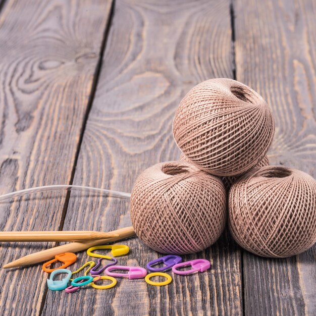 Clews of yarn, knitting needles and clips on wooden space.