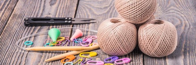 Clews of yarn, knitting needles, scissors and clips on wooden background.