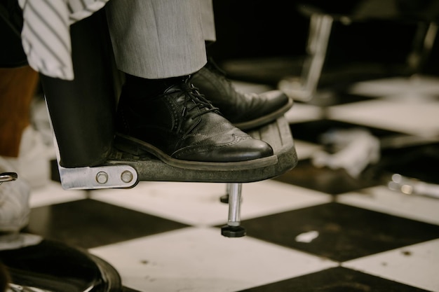 Foto cliënt benen in een kapper op een stand in een stoel close-up. benen in zwarte leren schoenen