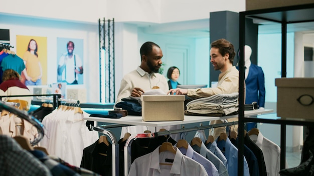 매장에 걸려 있는 옷을 보고 있는 고객과 직원, 젊은 남성이 새로운 패션 컬렉션을 구입할 수 있도록 도와주는 소매 조수. 옷장, 세련된 라이프 스타일을 개선하려는 남성 고객.