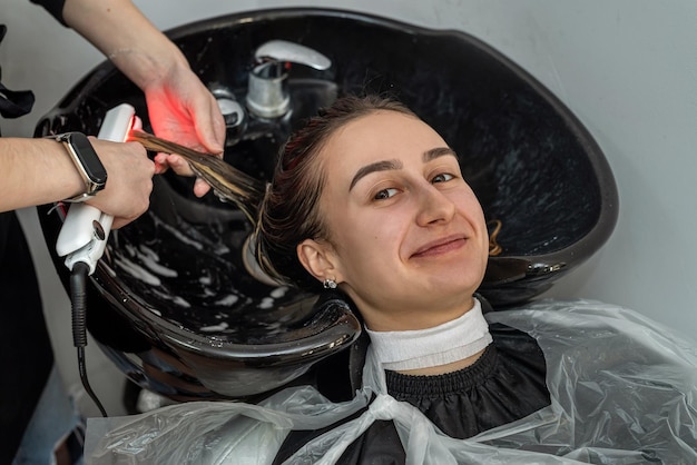 彼女の頭がプロのマスターによって洗われるとき、クライアントの女の子は美容院で微笑む