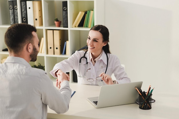 Client and smiling doctor shaking hands in medical office