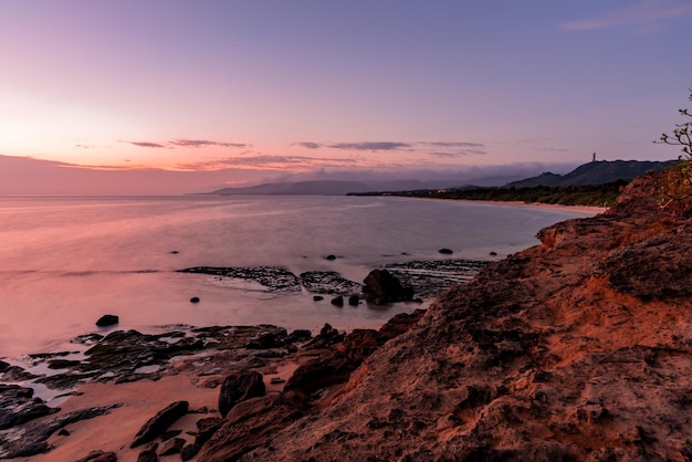 Photo cliff view of a peaceful dawn at the island beach mountains coastal rocks colorful lilac pink sky