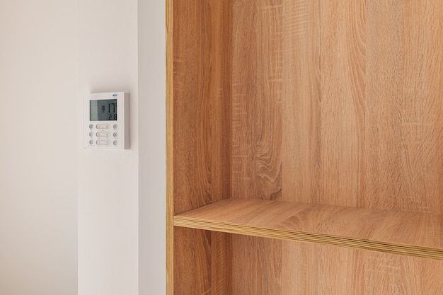 Climate control panel on the wall in a room with wooden builtin furniture with shelves