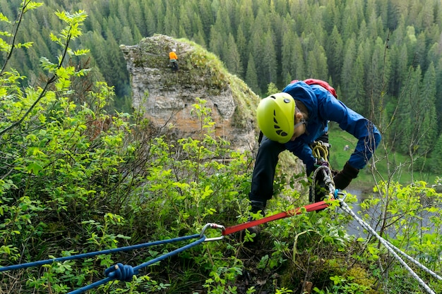 Climber girl checks the safety equipment while preparing to descend from the cliff above the river