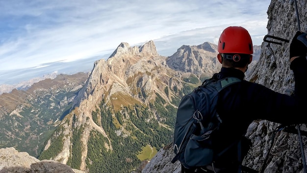 Photo climber man in a helmet on the top of a mountain looking into the horizon view from the back