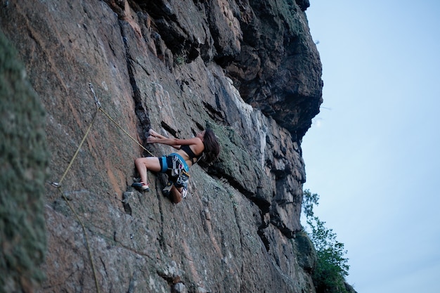 Climber overcomes challenging climbing route. A girl climbs a rock. Woman engaged in extreme sport. Extreme hobby. view from afar, a girl climbs with a lower rope