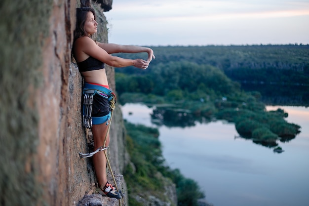 クライマーは挑戦的な登山ルートを克服します。女の子が岩を登る。エクストリームスポーツに従事する女性。極端な趣味。女性はチップに背を向けて立ち、休息し、筋肉を伸ばします