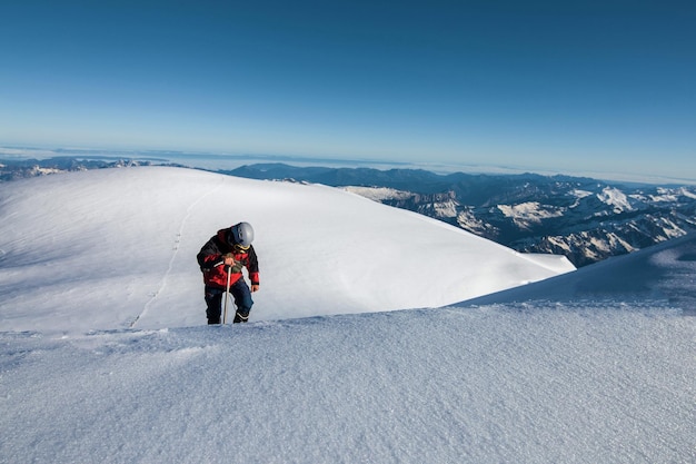 Альпинист в красной куртке взбирается на гору на фоне голубого небаxD