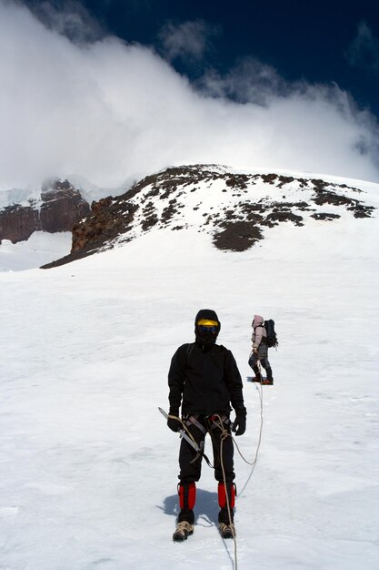 雪に覆われた氷河のそばを登り、高い頂上まで登る登山者