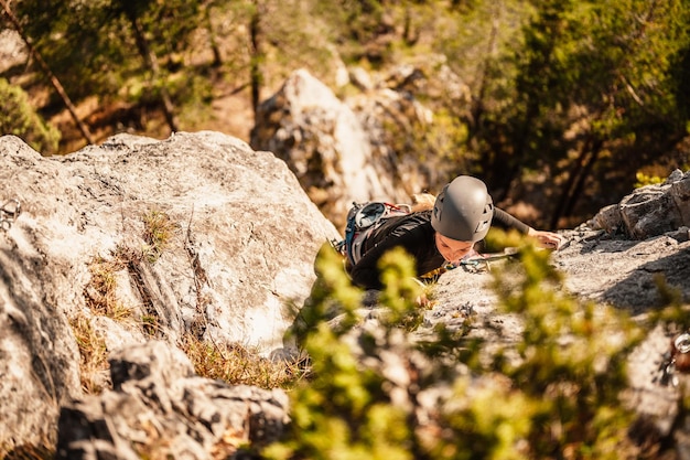 登山用具を身に着けているクライマー 岩山の壁でロッククライミングを練習する クライミングスポーツとボルダリングのコンセプト ロッククライマーが岩壁を登る