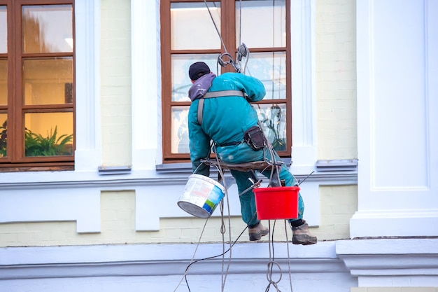 Climber worker is engaged in the repair and cleaning of windows and the facade of a renovated residential building construction business industry