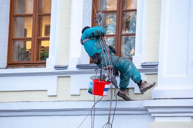 Climber worker is engaged in the repair and cleaning of windows\
and the facade of a renovated residential building construction\
business industry